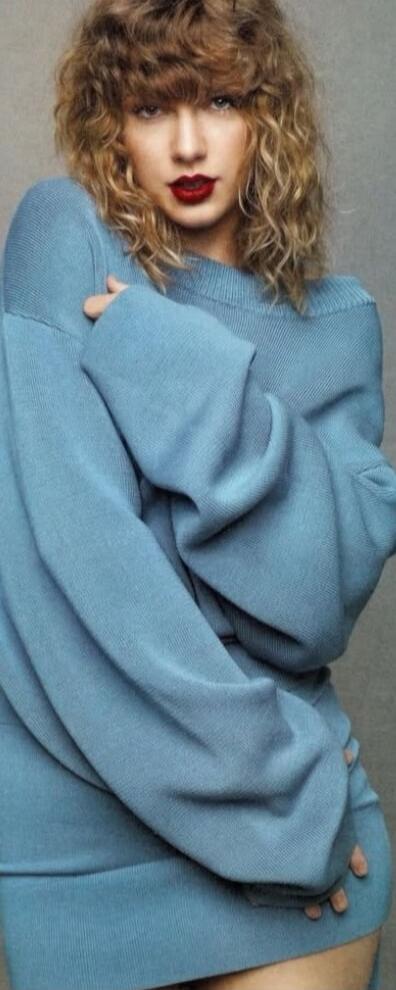 A woman in a light blue oversized sweater posing with curly hair and red lipstick.