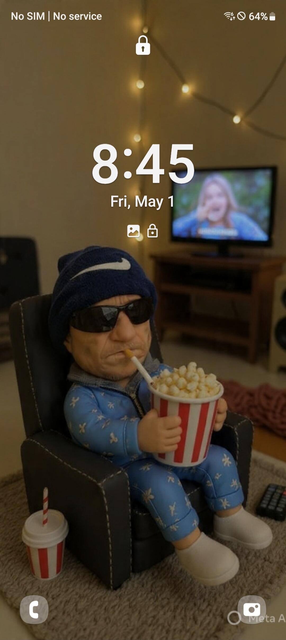 No SIM | No service 8:45 Fri, May 1 64% C Meta AI. A figurine resembling a man in a Nike beanie, sunglasses, and blue pajamas is sitting in a chair, holding a bucket of popcorn and smoking a cigarette. In the background, a TV shows a blurry image of a person.