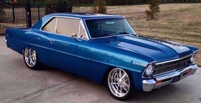 A classic blue car with chrome wheels is parked on a paved surface.