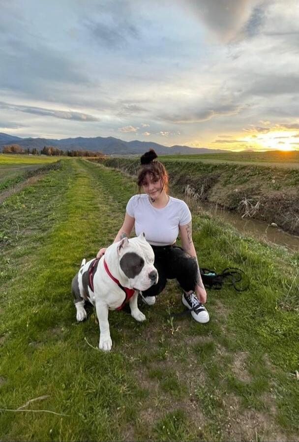Woman with a dog on a grassy path in a rural field at sunset.