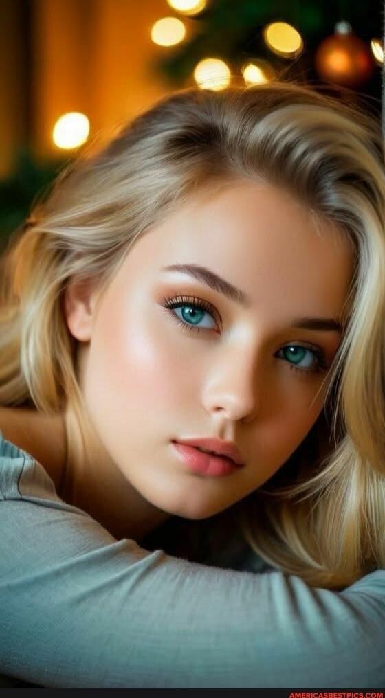 Portrait of a young woman with blonde hair and blue eyes, resting her head on her arms.