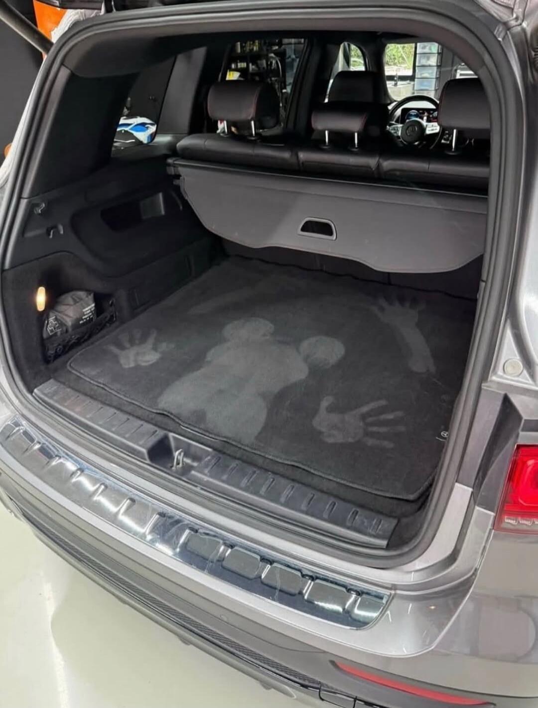 Car trunk interior with cargo mat featuring footprint imprints.