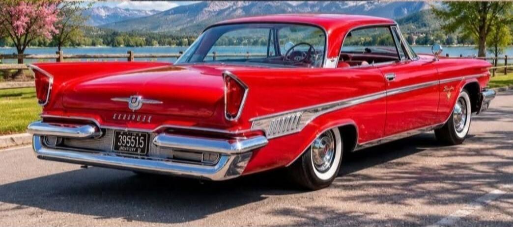 A red vintage car with a Kentucky license plate '395515' is parked by a lake with mountains in the background.