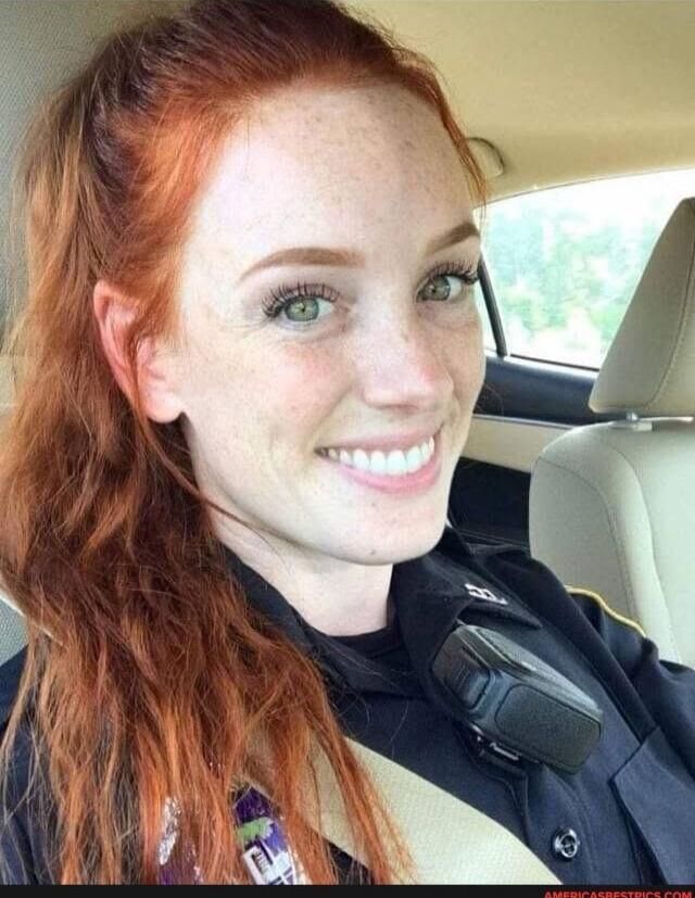 Smiling woman in a police uniform inside a car.