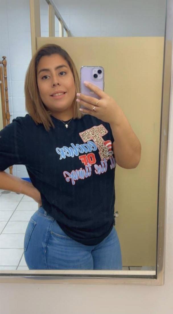 Mirrored text on t-shirt: 'GOODNESS OF THE THING' (with leopard print 'T'). A woman is taking a mirror selfie.