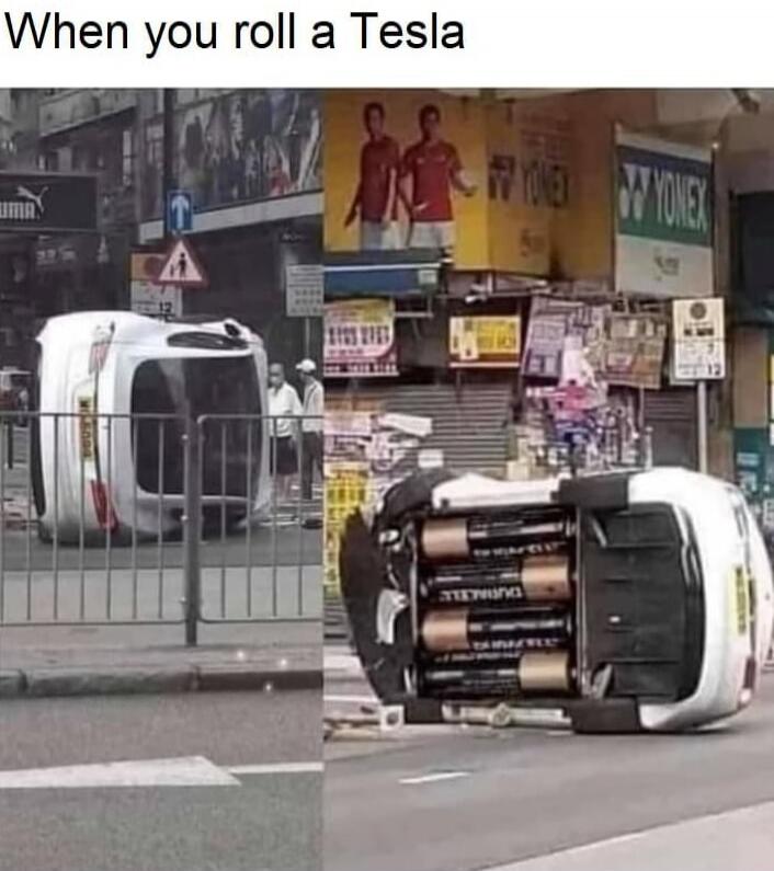 When you roll a Tesla. A white car is overturned on a city street, and its underside reveals several large Duracell batteries arranged inside.