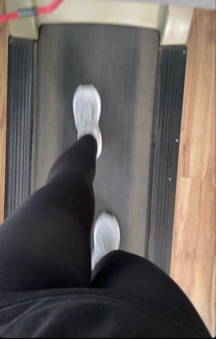 A person walking on a treadmill wearing white sneakers and black leggings.