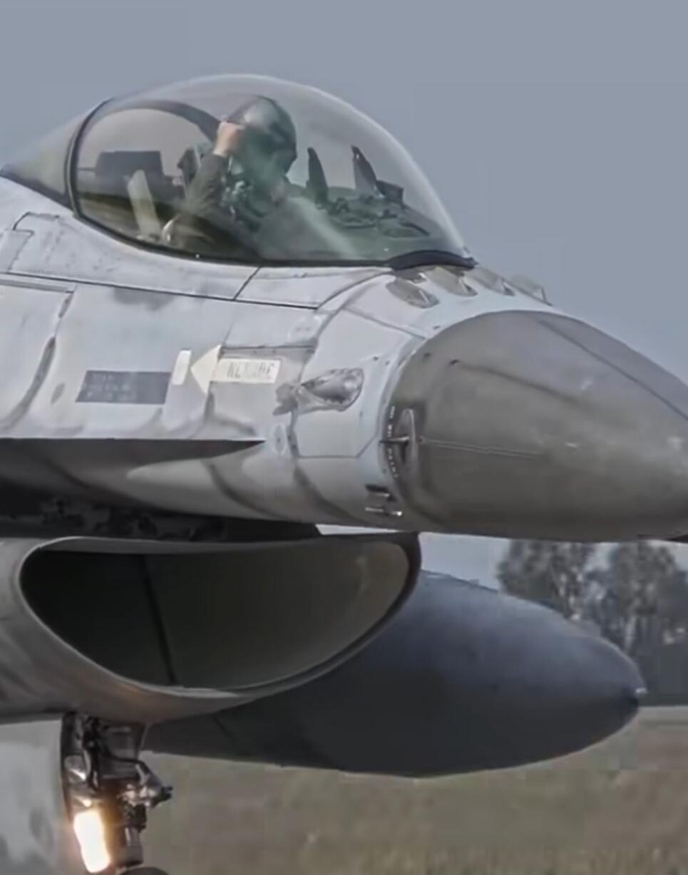 A pilot in the cockpit of an F-16 fighter jet. The word 'RESCUE' is visible on the side of the aircraft.