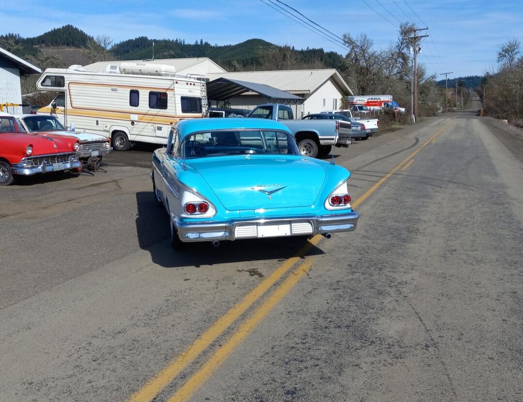 U-HAUL. A light blue vintage car is parked on the side of a road, with other vehicles and buildings in the background.