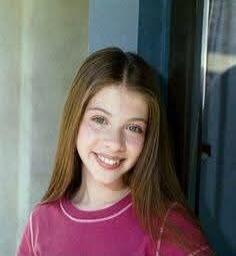 A young girl smiling in a pink shirt.