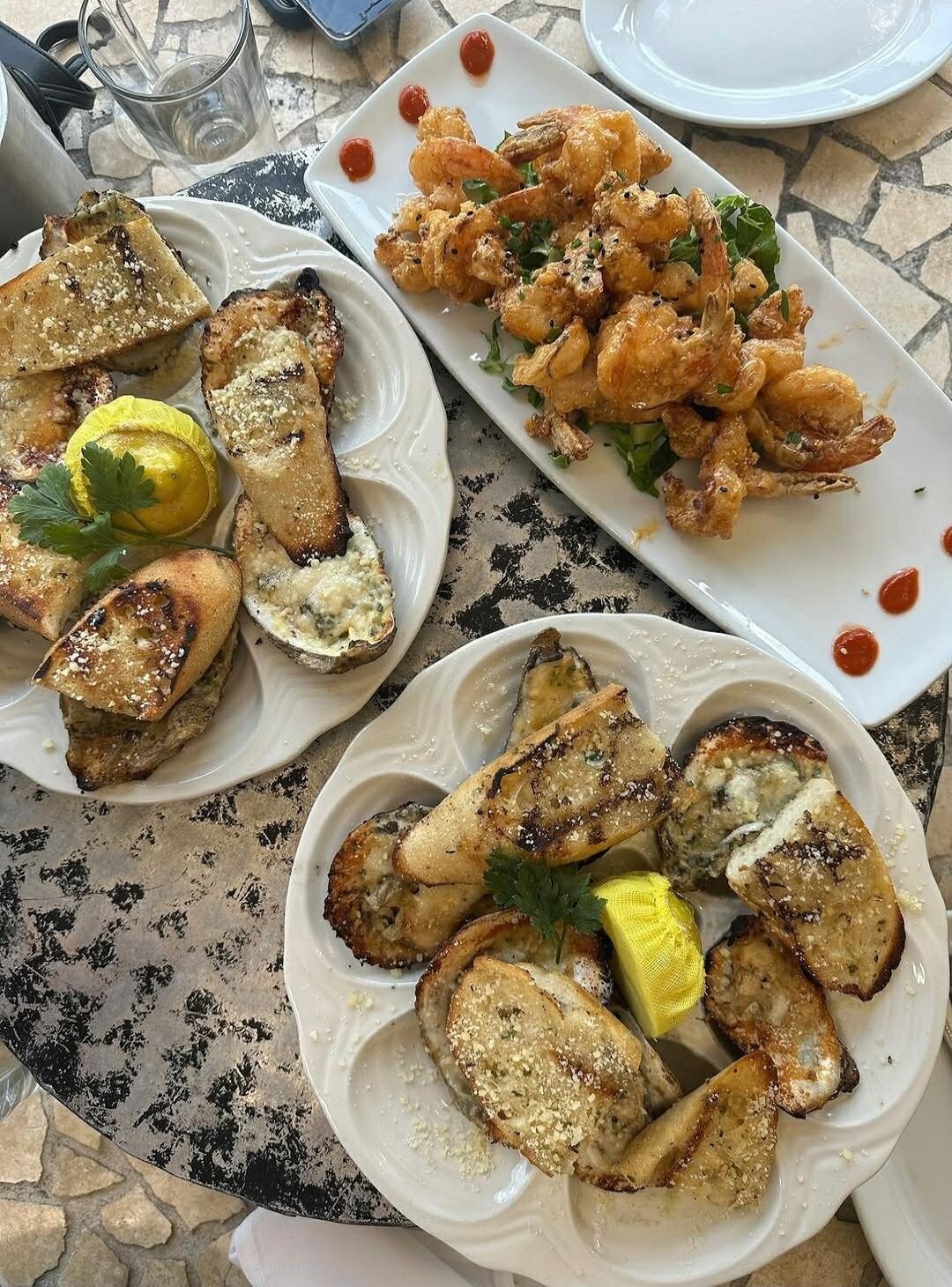 There are two plates of food. One plate has fried shrimp. The other plate has oysters and bread. There is also a lemon wedge and parsley on the plate with oysters and bread.