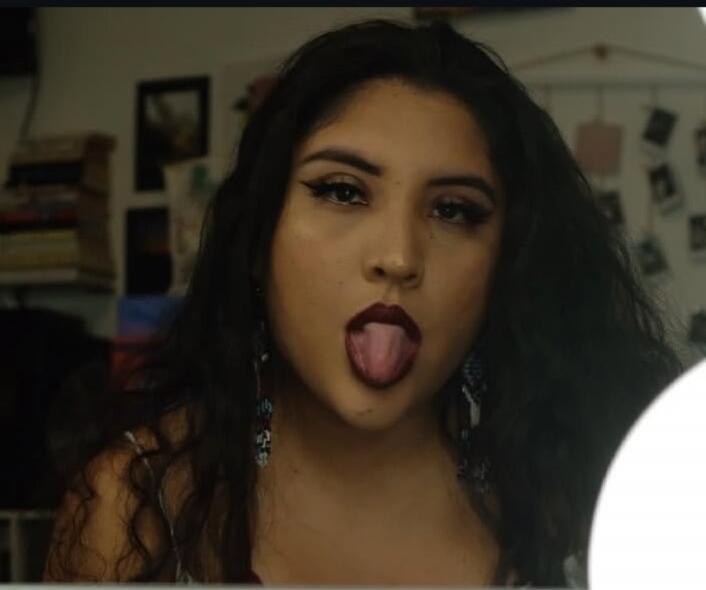 A young woman with dark hair and makeup sticking her tongue out.