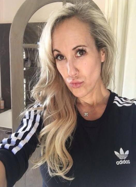 A woman wearing a black Adidas sweatshirt with white stripes on the sleeves, taking a selfie. The Adidas logo is visible on her shirt.