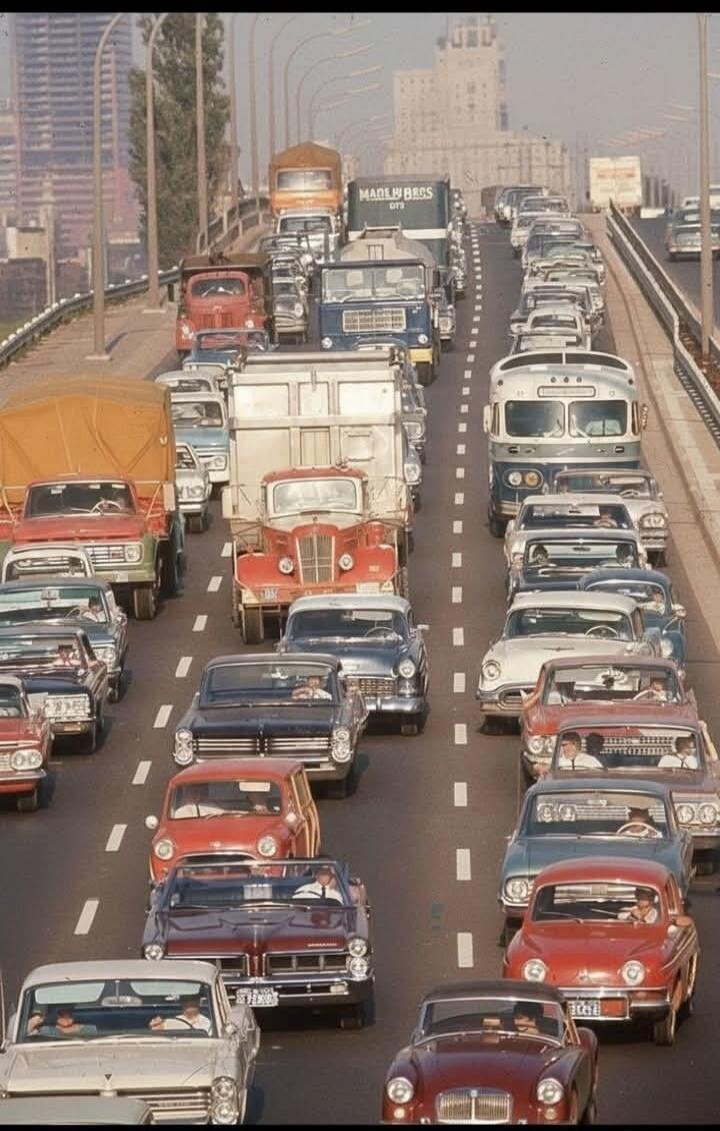 A busy multi-lane highway filled with numerous vintage cars and trucks in heavy traffic.