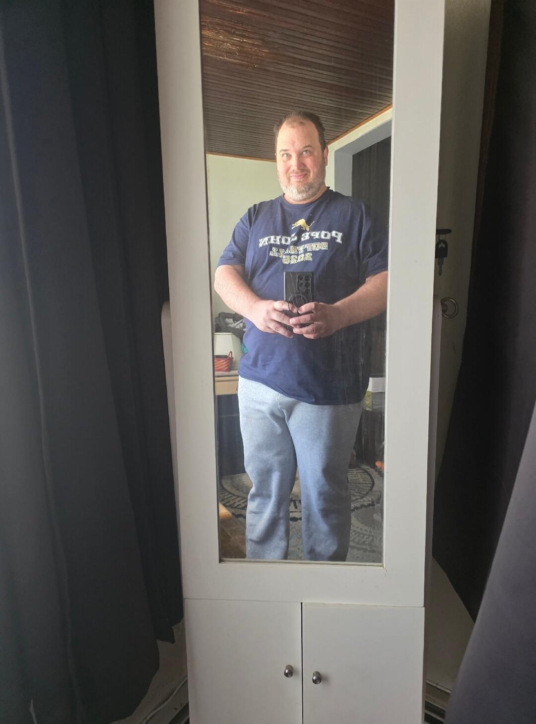 A man taking a mirror selfie. The text on his t-shirt reads 'POPE JOHN PAUL II'.
