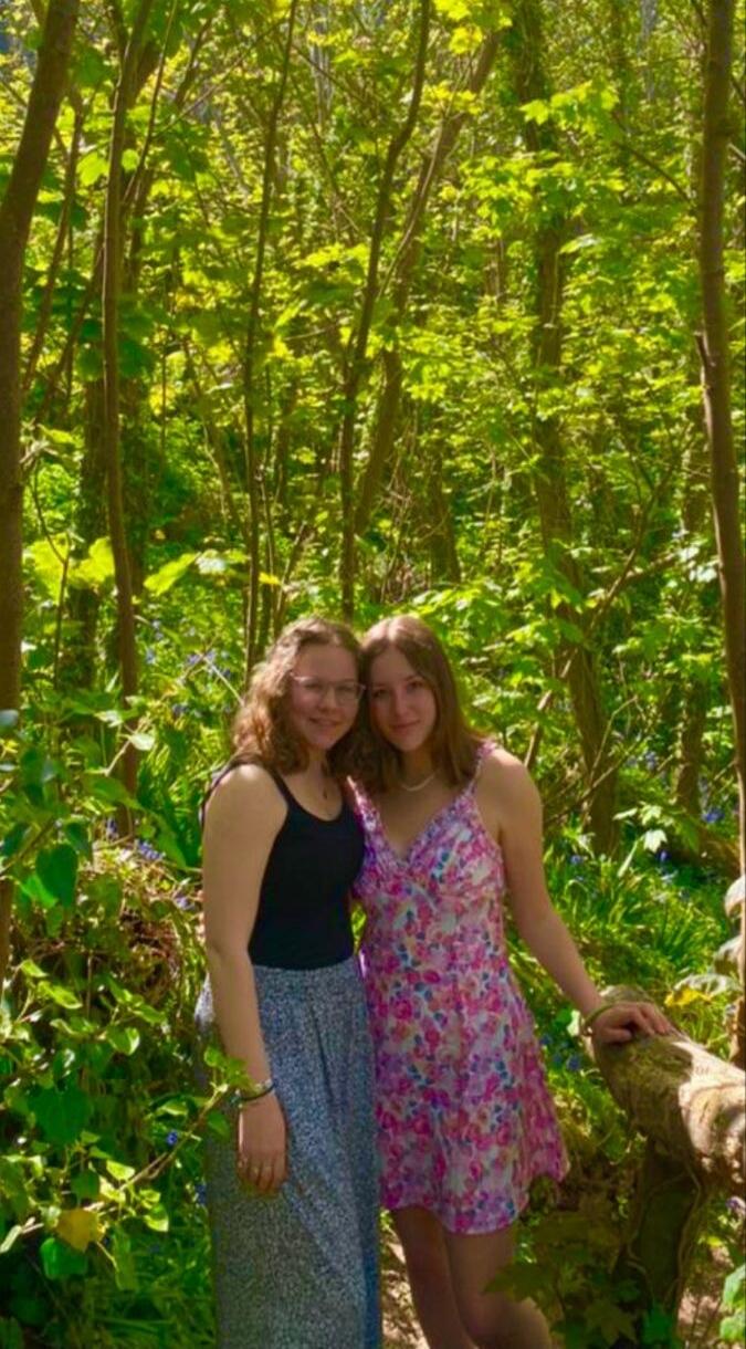 Two young women smiling in a vibrant green forest.