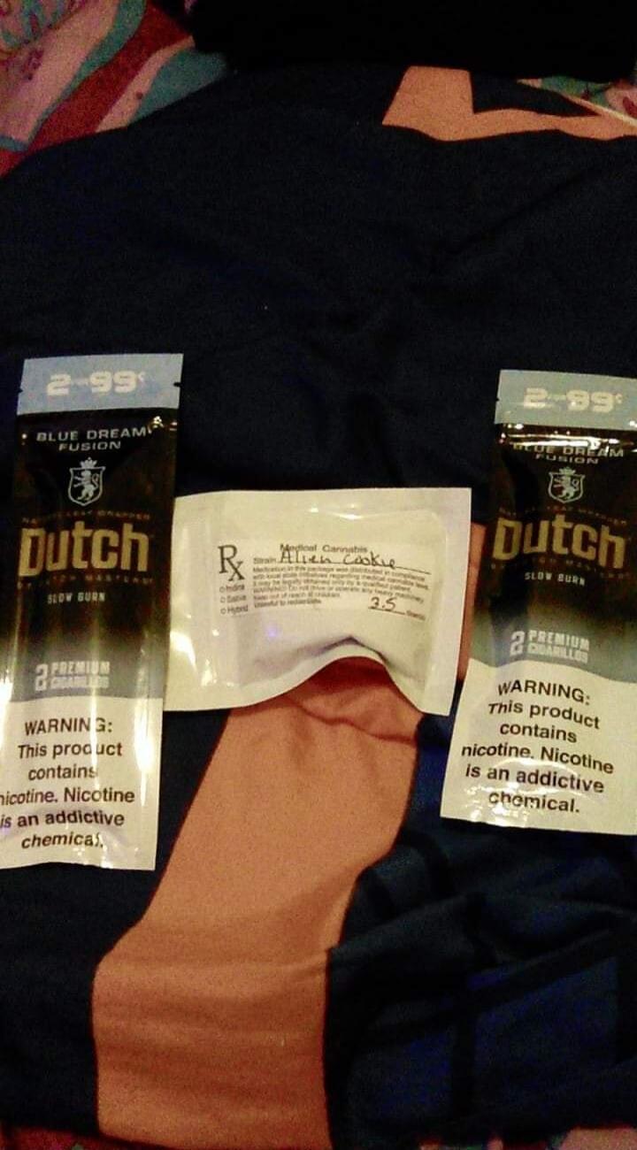 Two packages of Dutch Blue Dream Fusion Slow Burn Premium Cigarillos, priced at 2.99 each. Both packages carry a warning: 'This product contains nicotine. Nicotine is an addictive chemical.' In the center, there is a small white package labeled 'Medical Cannabis' with the strain 'Alien Cookie' and a handwritten '2.5'.