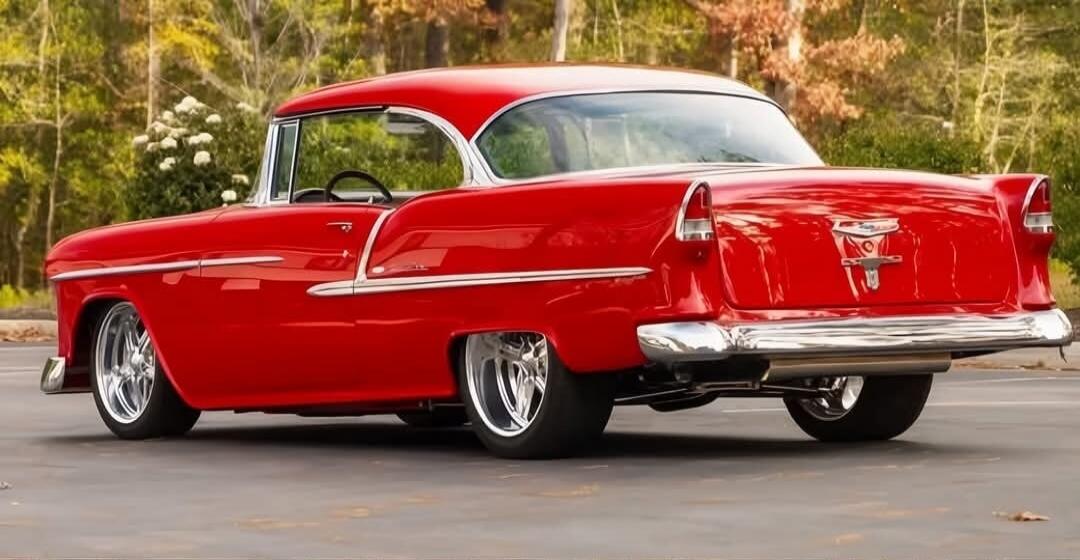 A red vintage car parked on a paved area with trees in the background.