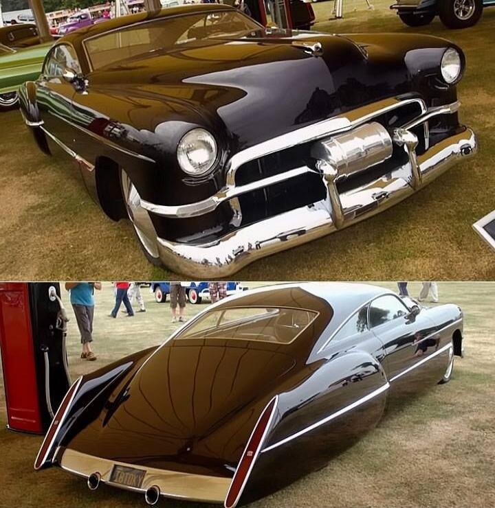 A custom-built, dark-colored vintage car with a low stance and chrome accents, displayed on a grassy field. The license plate reads '18TOKY'.