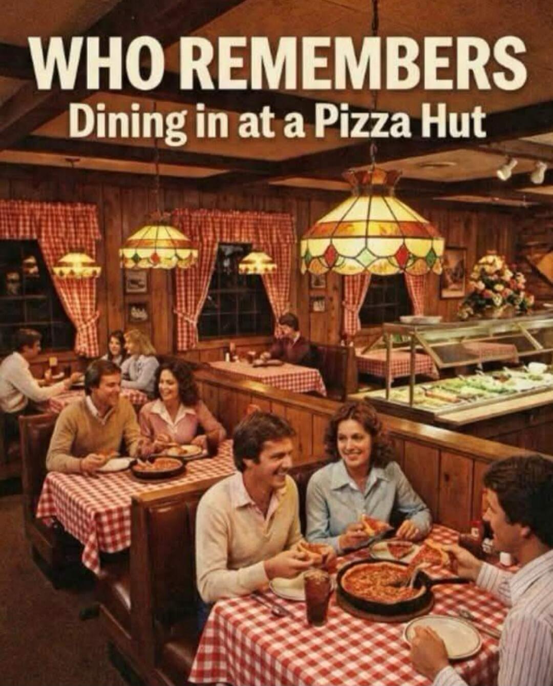 WHO REMEMBERS Dining in at a Pizza Hut. A vintage photo showing people dining inside a classic Pizza Hut restaurant with wood paneling, checkered tablecloths, and stained-glass lamps. People are eating pizza and smiling, with a salad bar visible in the background.