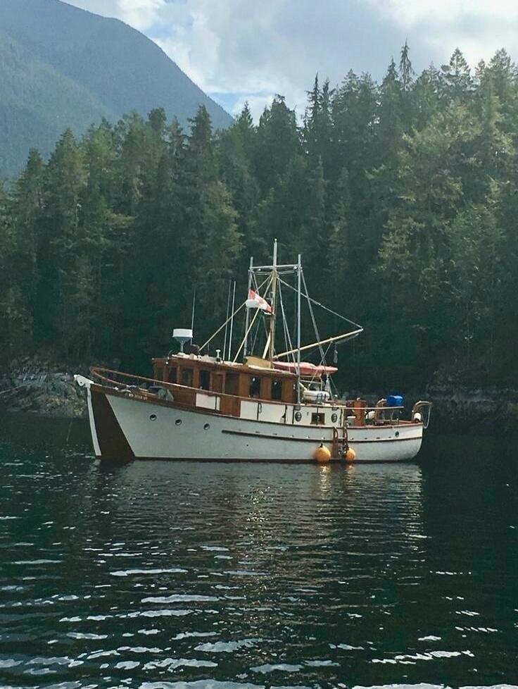 A classic wooden boat anchored on calm water near a forested shoreline.