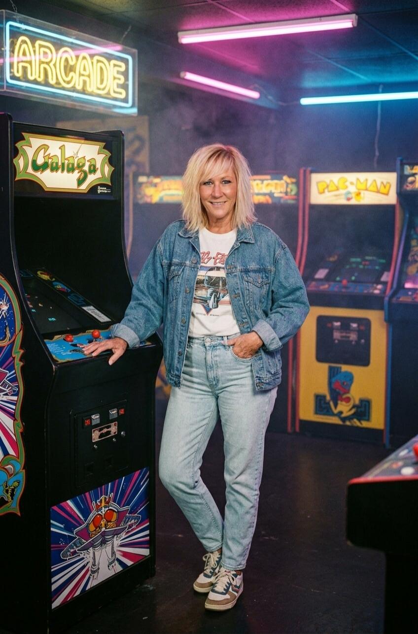 A woman stands in an arcade next to a Galaga machine. Neon signs for 'ARCADE' and 'PAC-MAN' are visible in the background.