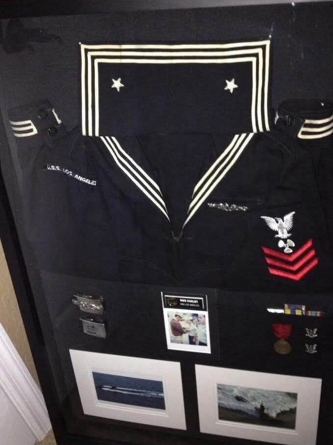 U.S.S. Los Angeles on left sleeve, naval insignia patches, eagle emblem with red chevrons, various medals, framed photos of ships, and other military memorabilia.