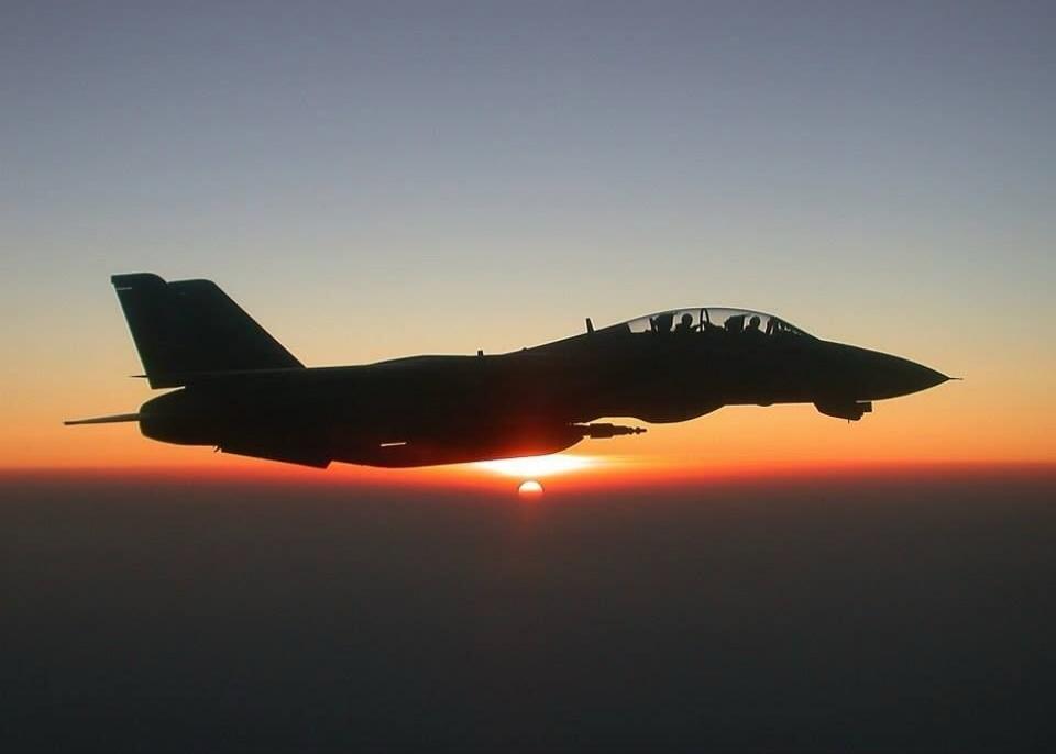 Silhouette of a fighter jet flying at sunset.