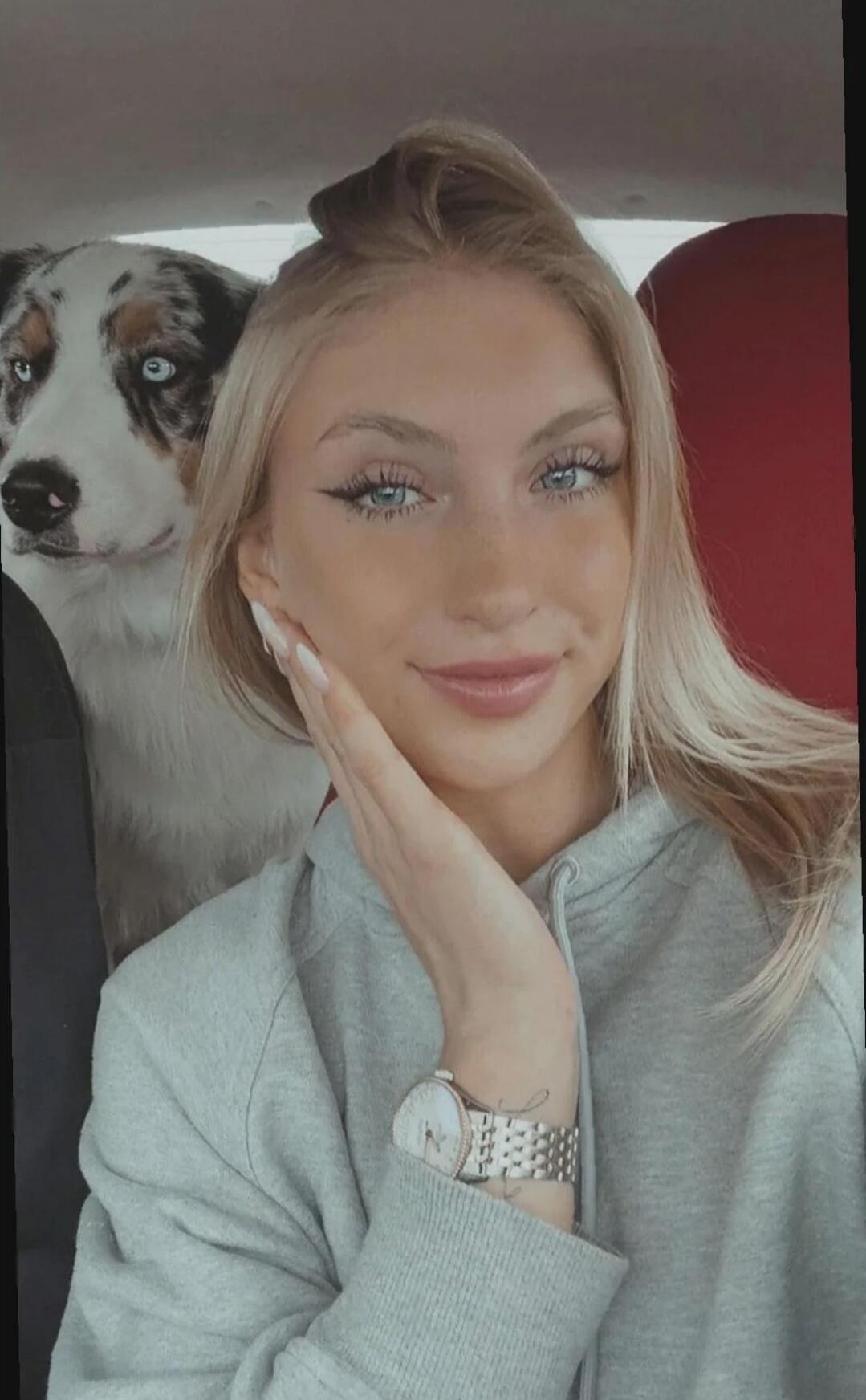 A young woman in a car with a dog in the back seat.