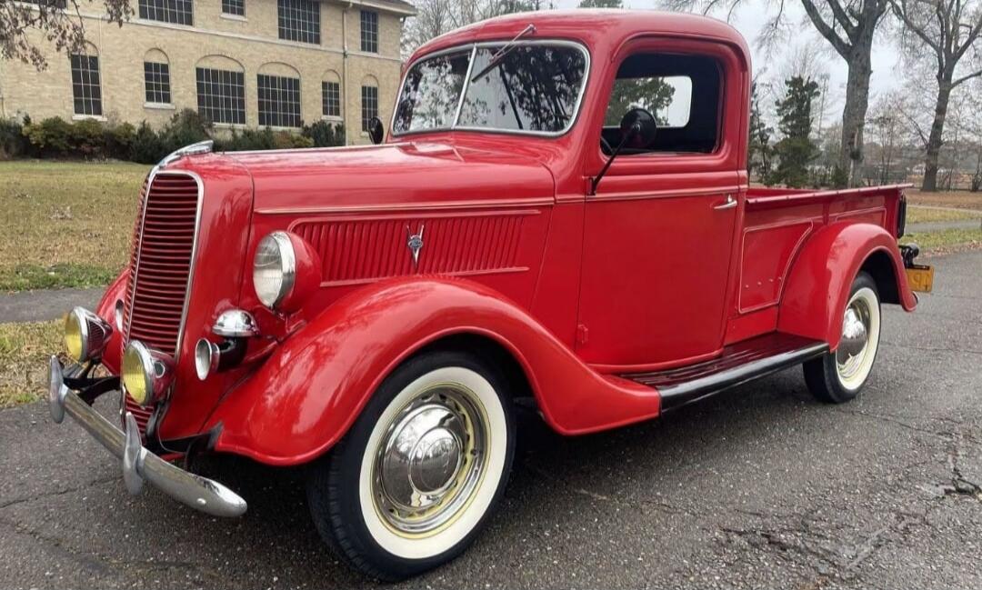 A classic red vintage pickup truck parked on an asphalt road in front of a building.