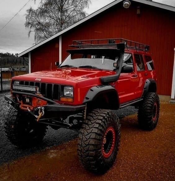 Red lifted Jeep with oversized mud tires and roof rack.