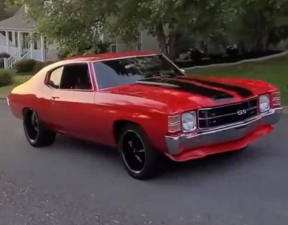 A red Chevrolet Chevelle SS with black racing stripes is parked on a street.