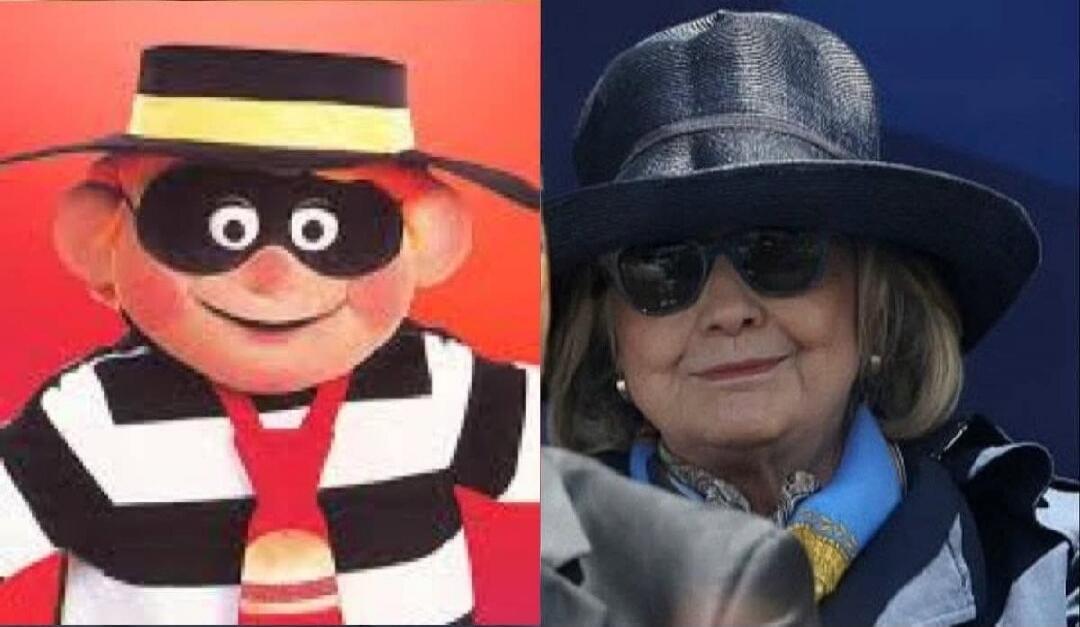 A split image showing the McDonald's character Hamburglar on the left and Hillary Clinton on the right. Hamburglar is depicted in his classic black and white striped outfit, mask, and hat. Hillary Clinton is wearing a dark hat and sunglasses, with a blue scarf.