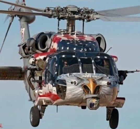 A military helicopter painted with an American flag design featuring an eagle face on the front.
