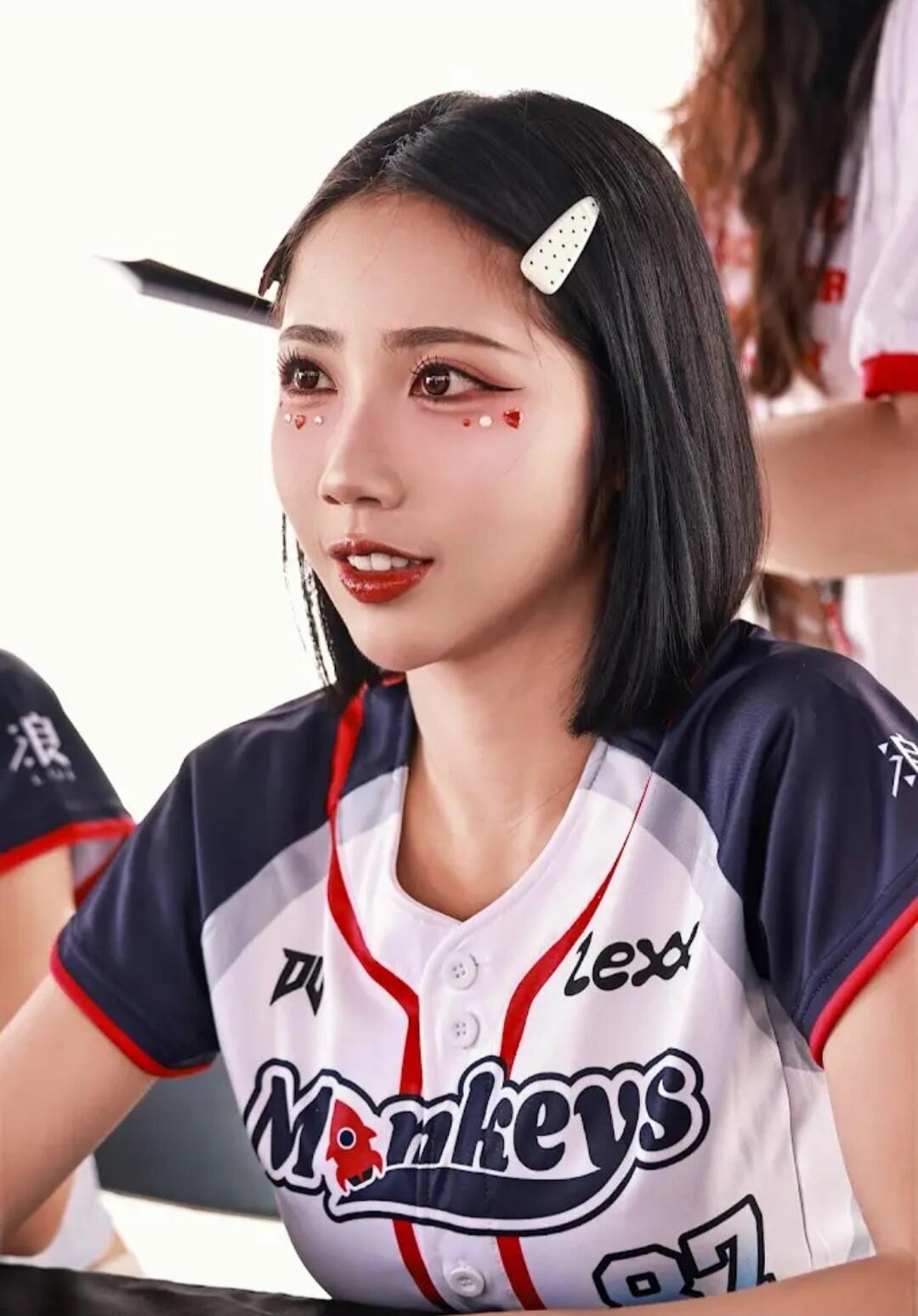 A young woman wearing a baseball jersey with 'Monkeys' and 'Lexd' written on it. She has elaborate eye makeup with red hearts and white dots, and a white polka-dot hair clip. The character '浪' is visible on her sleeve.