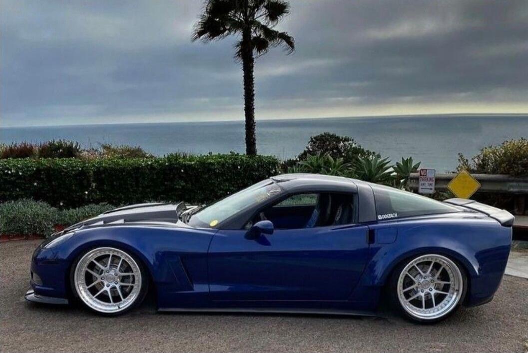 Blue sports car parked near the ocean with a palm tree in the background.