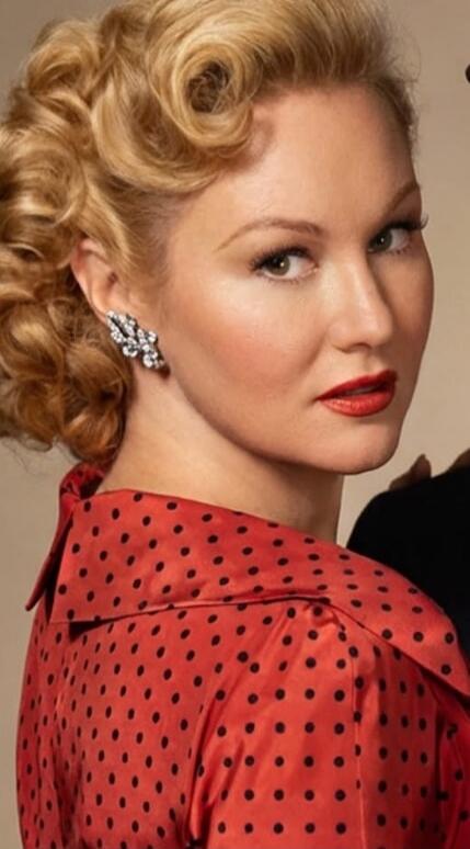 Portrait of a blonde woman wearing a red polka-dot blouse with a vintage hairstyle and red lipstick.