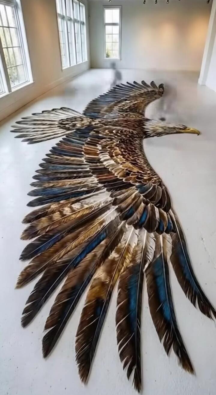 A large winged bird artwork spread across a white floor inside a room with windows.