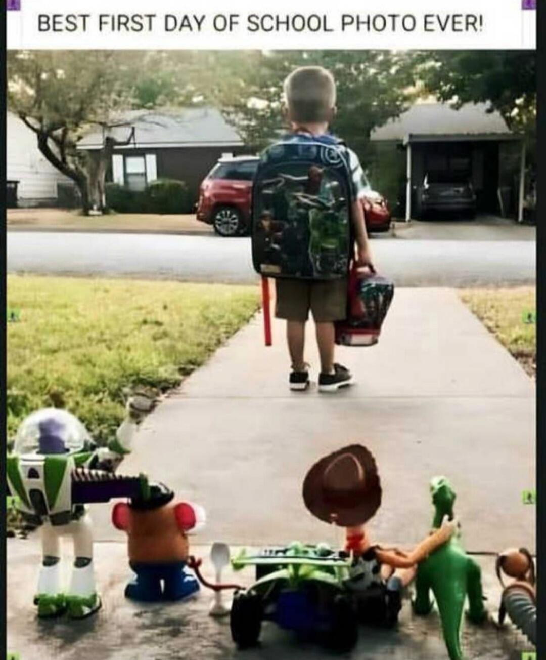 BEST FIRST DAY OF SCHOOL PHOTO EVER! A young boy with a backpack and lunchbox walks away on his first day of school, while his Toy Story action figures are arranged on the sidewalk as if waving goodbye to him.
