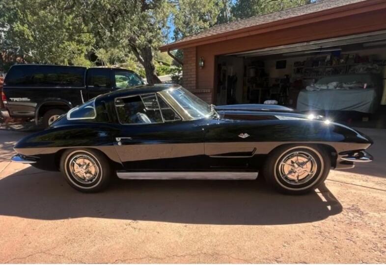 Black classic car parked in a driveway; appears to be a vintage mid-century sports car with chrome wheels and a sleek, aerodynamic profile.