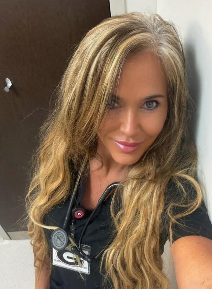 A blonde woman wearing black scrubs with a stethoscope around her neck, posing for a selfie.