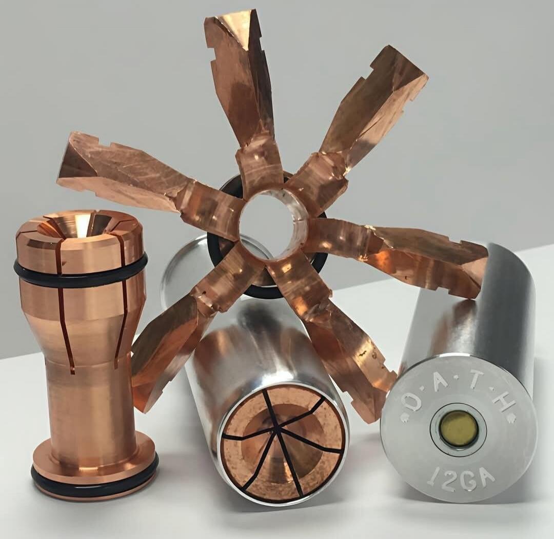 Circular metal rotor with copper spokes, copper cylindrical pieces, and a gray end cap with etched markings around the edge (appears to read '26GA'). A small copper barrel sits to the left.