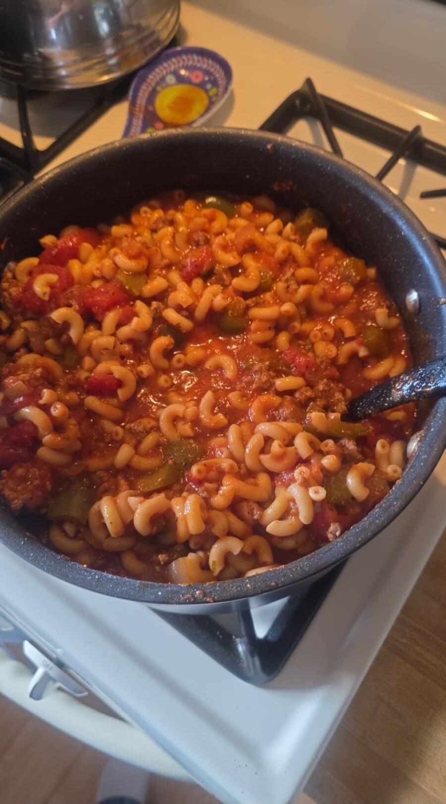 A pot of pasta shells in a chunky tomato sauce with vegetables (green peppers, corn, and possibly diced tomatoes) cooking on a stove.