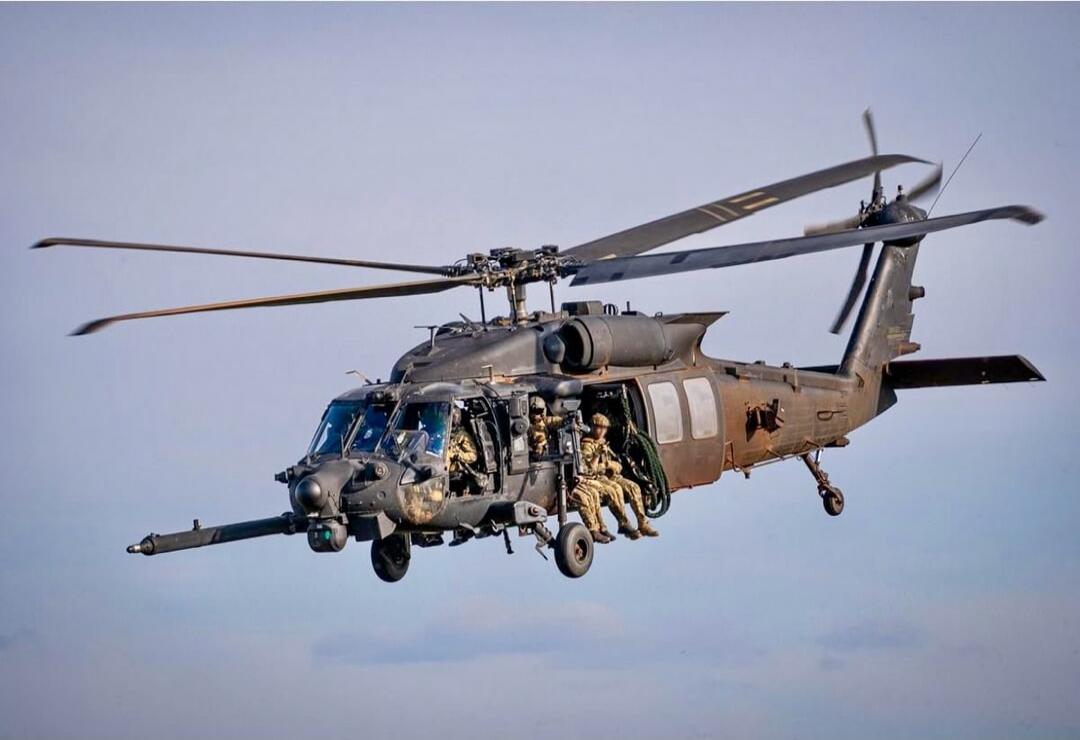 A military helicopter in flight with soldiers rappelling/boarding from the side.