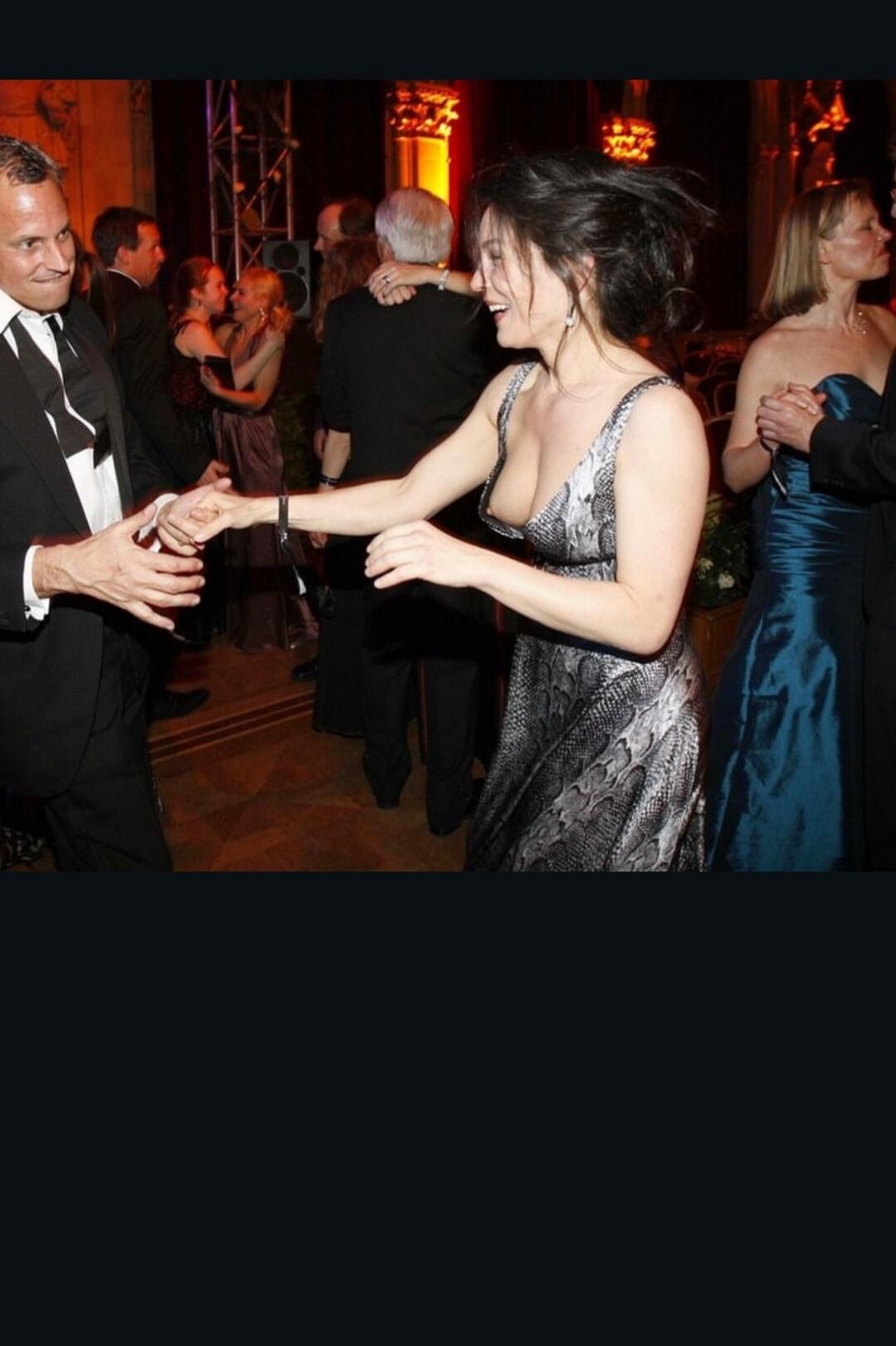Two people dancing at a formal event or gala, wearing evening attire and smiling while holding hands.
