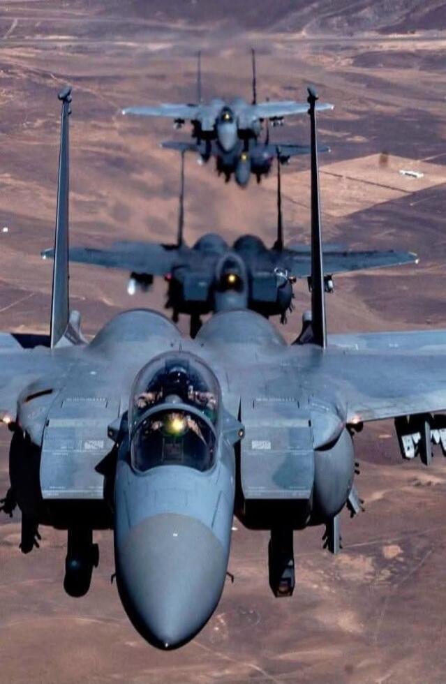 Two fighter jets in tight formation flying over a desert landscape.