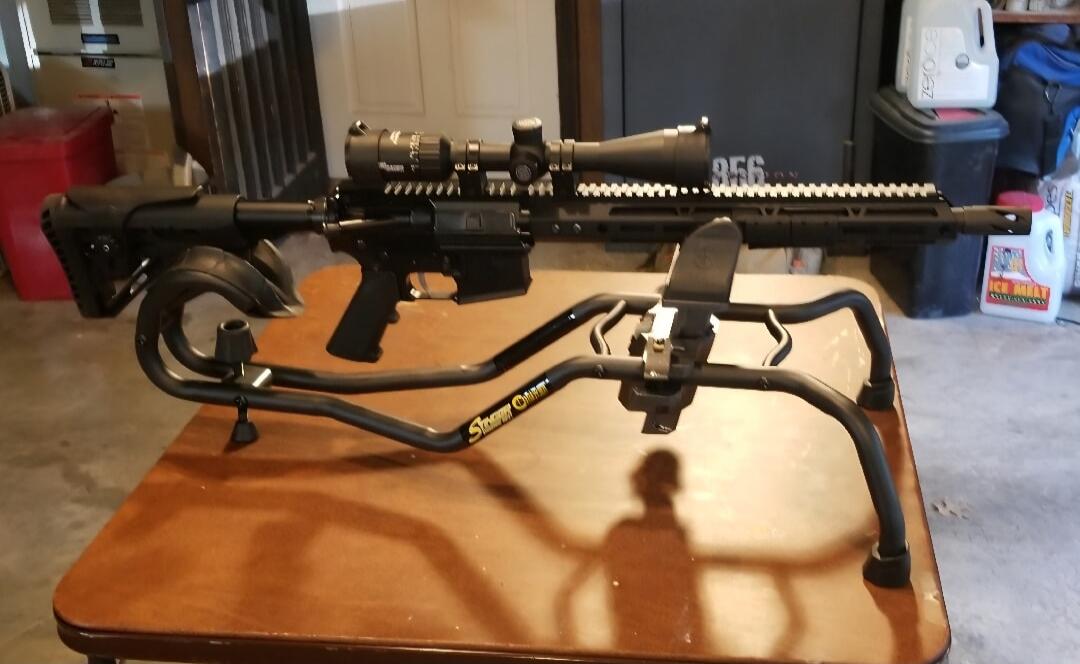 A rifle with a scope mounted on a bipod resting on a table.