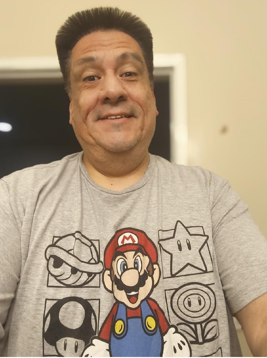 A man wearing a grey t-shirt with Super Mario Bros. characters and power-ups: Mario, a Koopa Shell, a Star, a Mushroom, and a Fire Flower.