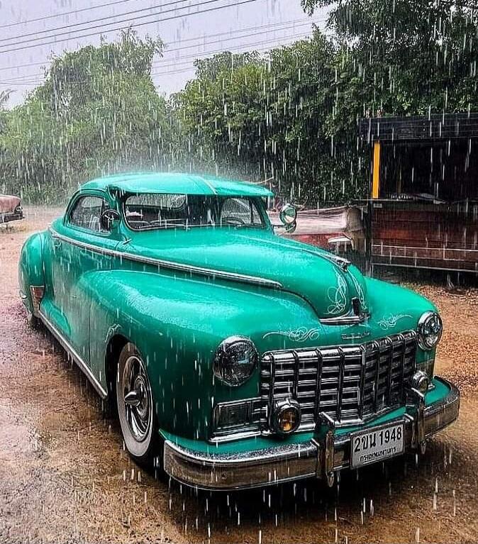 A vintage turquoise car parked in the rain.