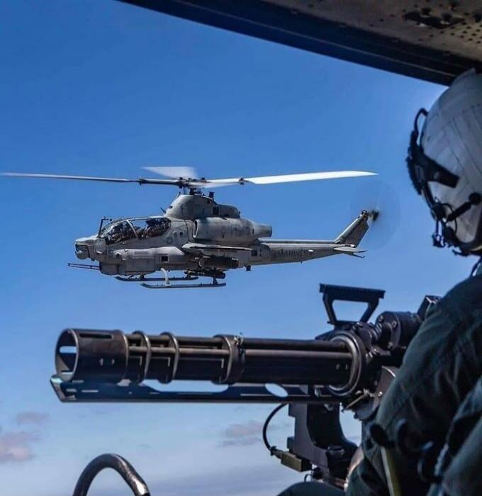 A military helicopter with a mounted gun and a gunner visible on a nearby aircraft.